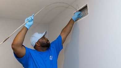 air duct cleaning worker inserting vacuum hose into vent